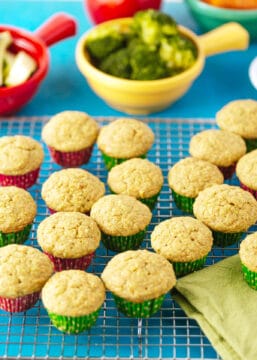 healthy fruit and veggie muffins on a cooling rack with broccoli and zucchini in the background