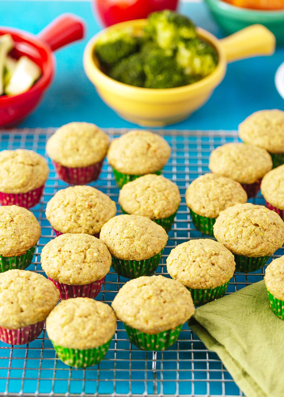 healthy fruit and veggie muffins on a cooling rack with broccoli and zucchini in the background