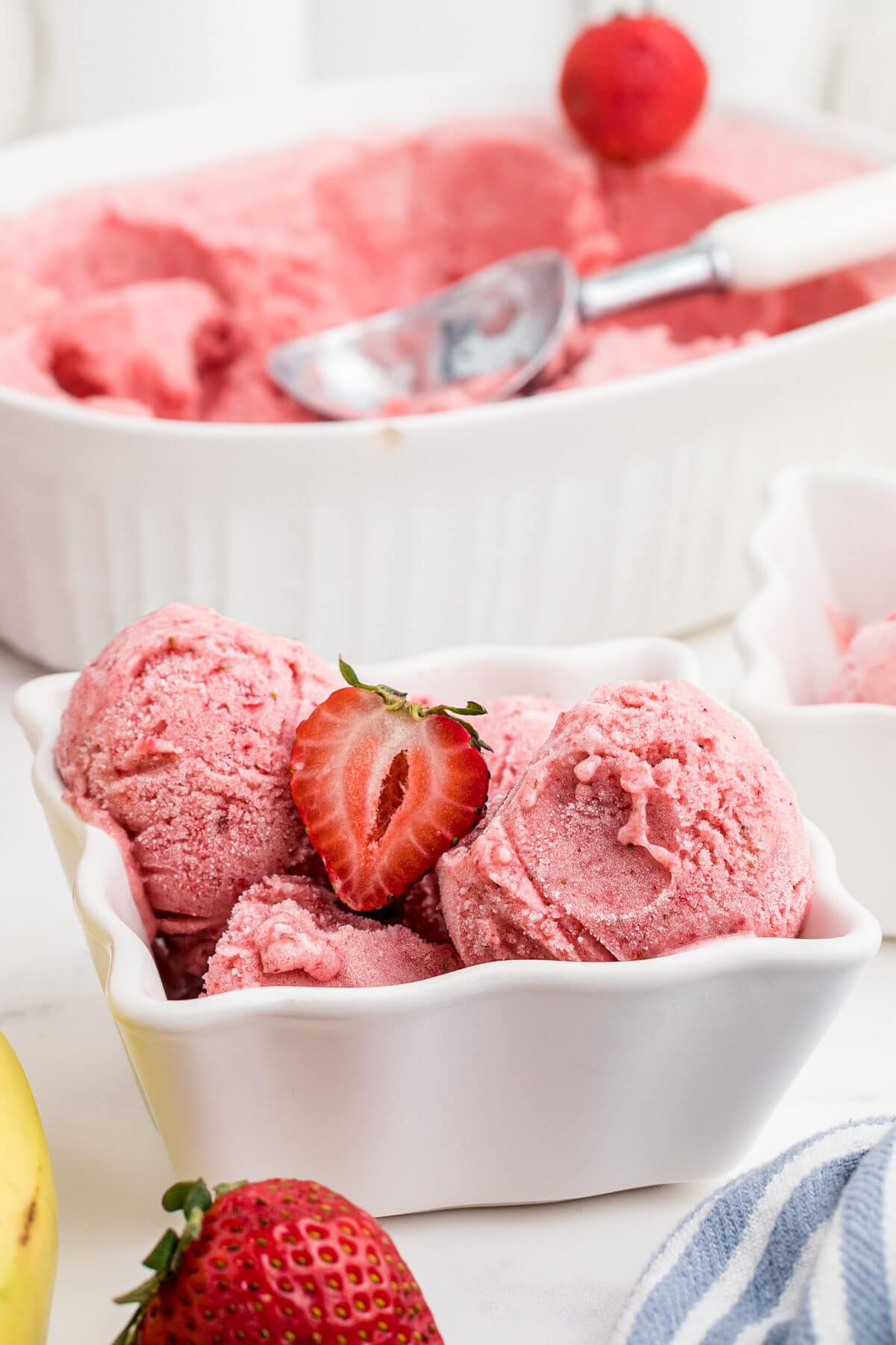 a white dish with scoops of strawberry banana frozen yogurt and fresh strawberries on top