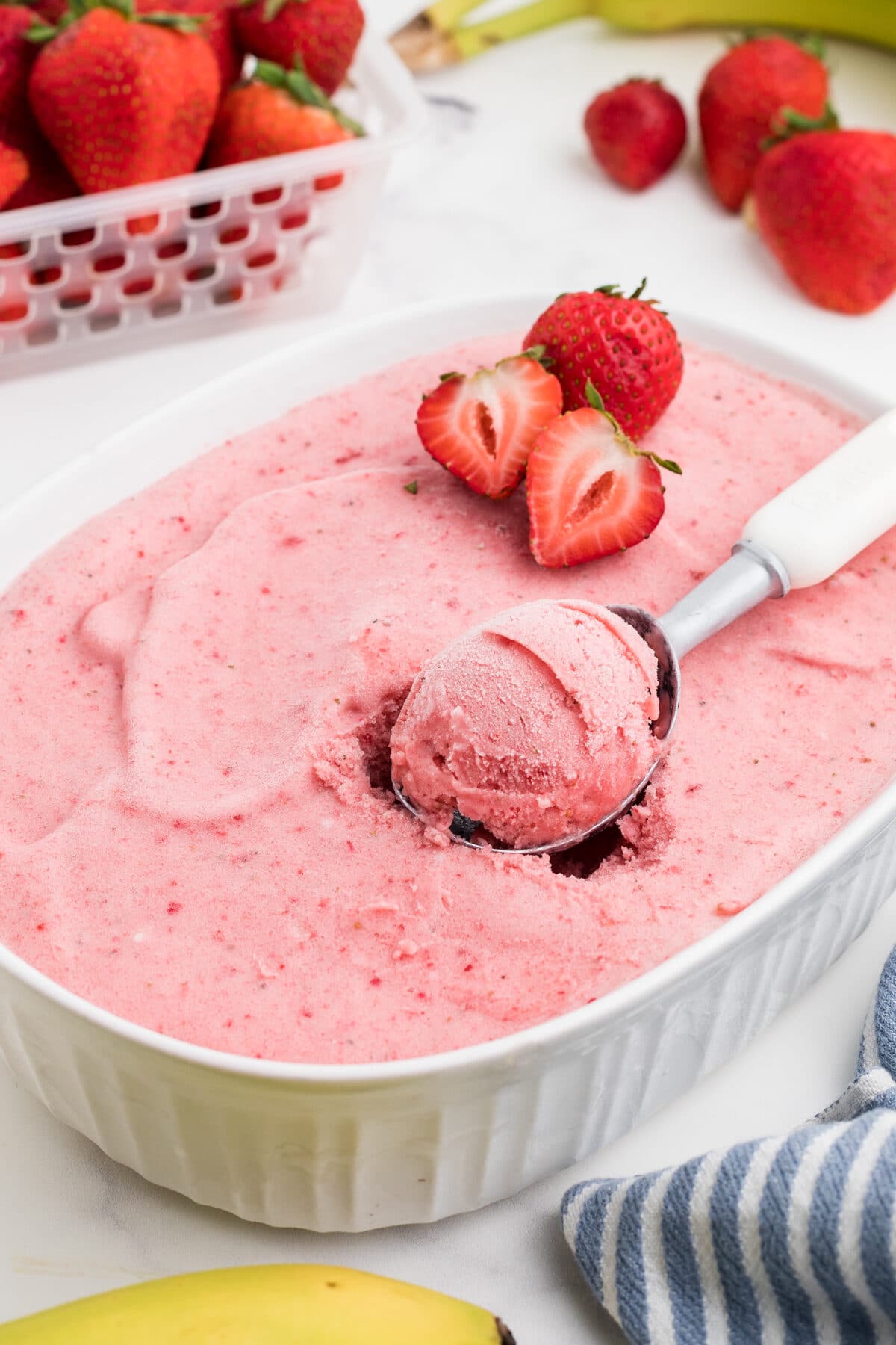 healthy strawberry banana frozen yogurt in a white glass dish with an ice cream scoop