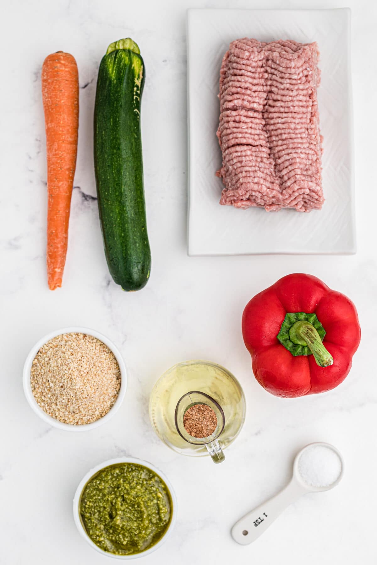 ingredients for baked chicken meatballs, ground turkey, carrot, zucchini, breadcrumbs, pesto, salt, olive oil