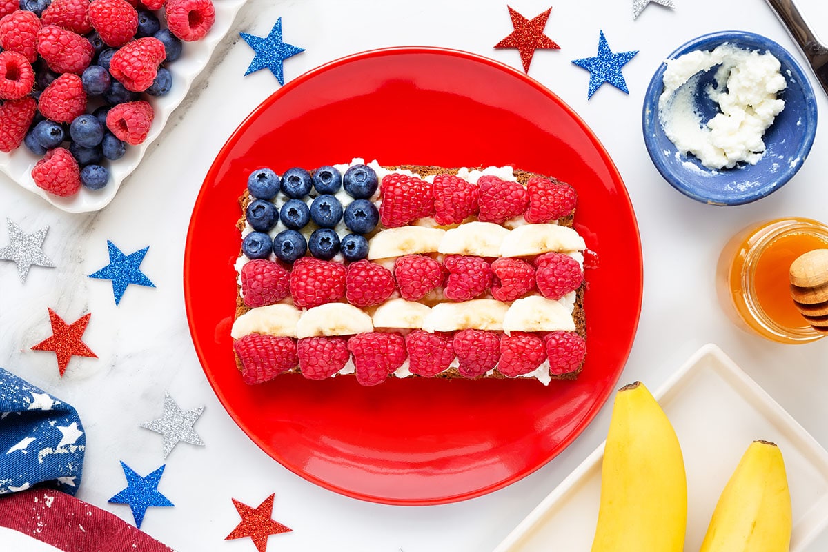 American flag ricotta toast with fresh fruit like raspberries, banana and blueberries on toast with patriotic decoration for Independence Day celebration