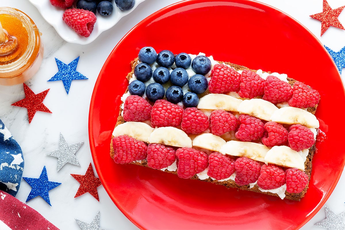 American flag ricotta toast with fresh fruit like raspberries, banana and blueberries on toast with patriotic decoration for Independence Day celebration