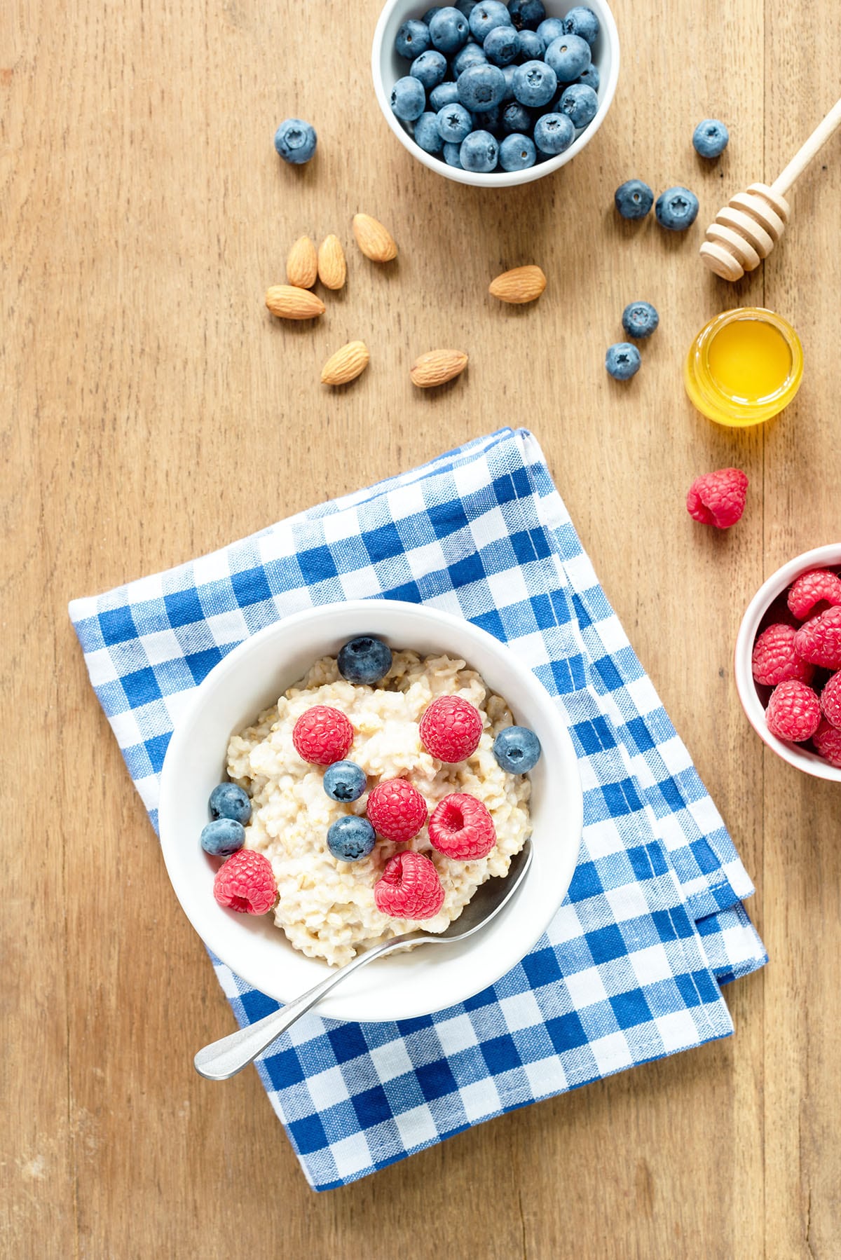 Breakfast table with oatmeal fresh berries and honey. Blue checked napkin under the bowl of oatmeal.