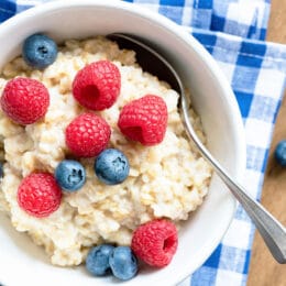 oatmeal with fresh berries in a white bowl with a blue checkered napkin underneath