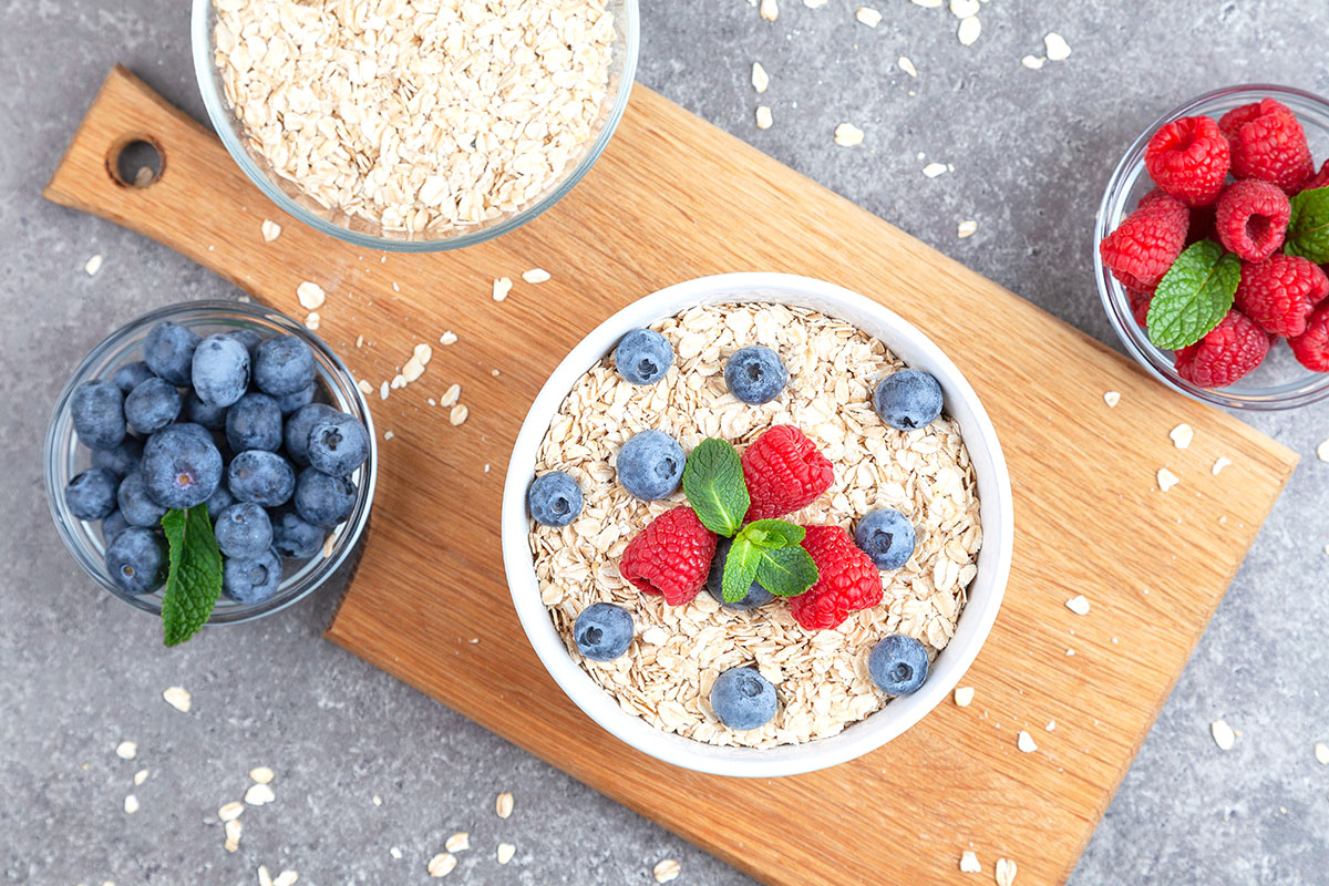 old fashioned oats in a bowl with fresh raspberries and blueberries in bowls and oats scattered on a wooden cutting board