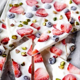 frozen yogurt bark on a parchment lined baking sheet with strawberries, blueberries, and pistachios