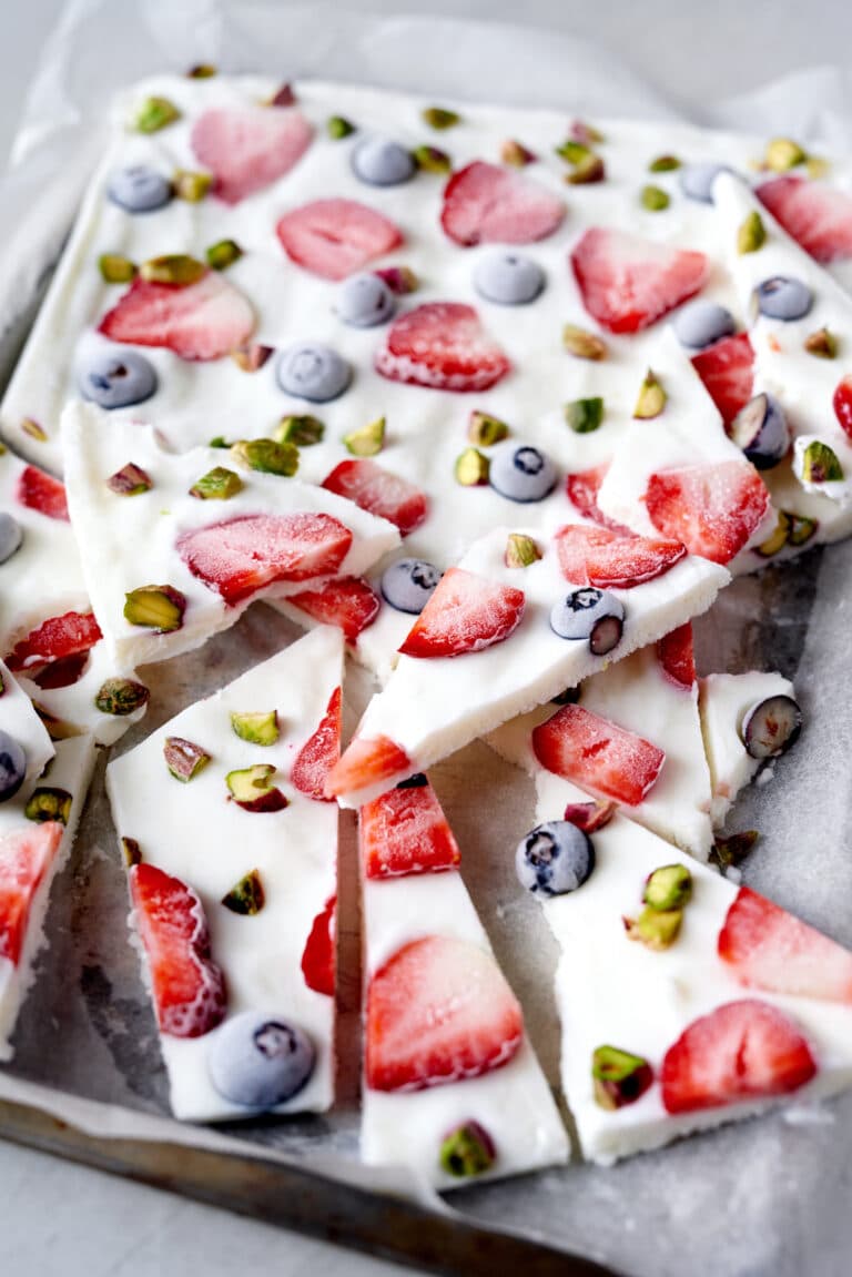 frozen yogurt bark on a parchment lined baking sheet with strawberries, blueberries, and pistachios