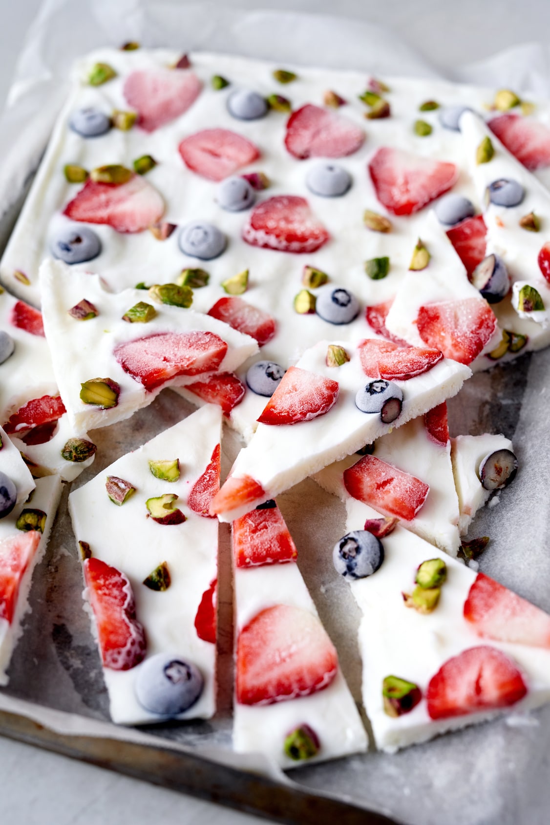 frozen yogurt bark on a parchment lined baking sheet with strawberries, blueberries, and pistachios