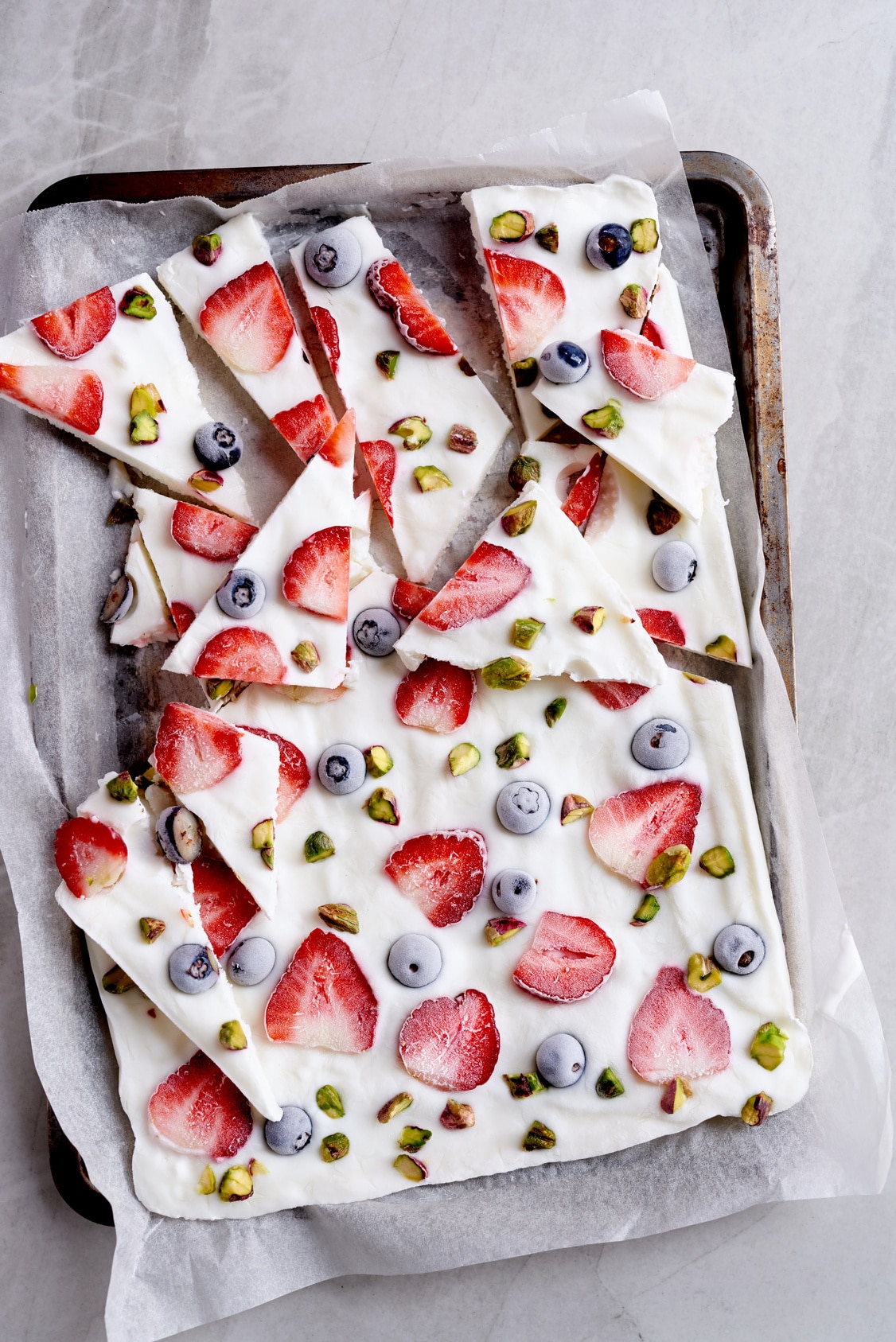 Frozen yogurt bark with strawberries, blueberries and pistachios on a parchment-lined baking sheet