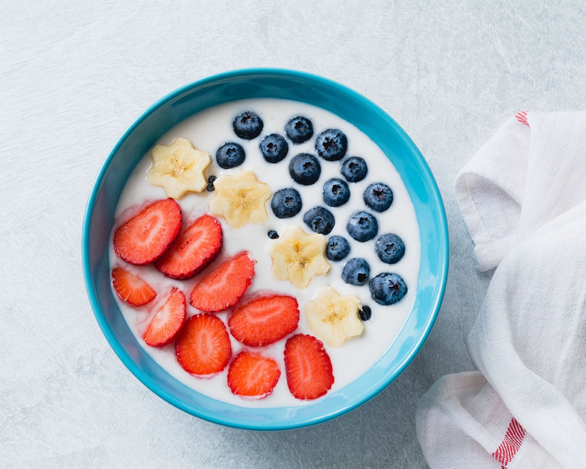 fruit and yogurt bowl with blueberries, strawberries, banana stars and granola in a blue bowl