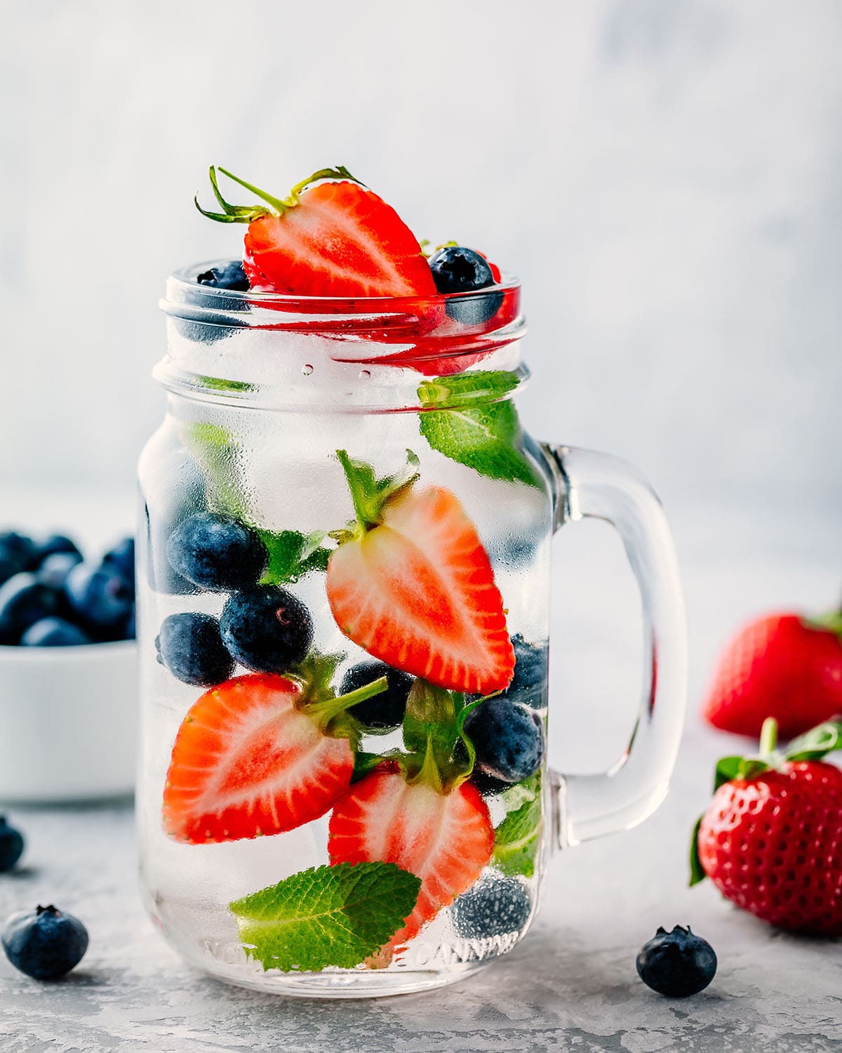 Infused fruit water with blueberry, strawberry and mint. Ice cold summer drink in glass mason jar