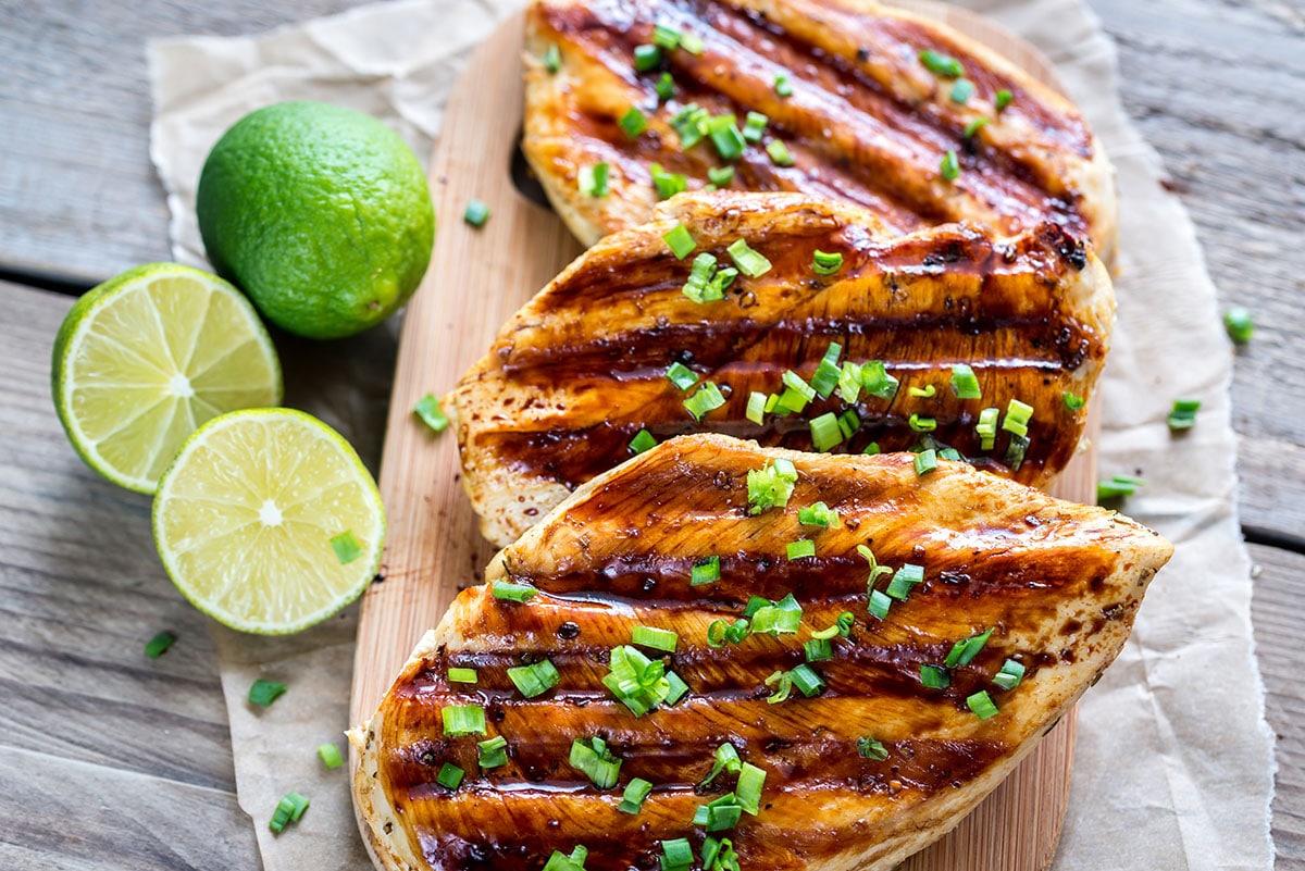 grilled chicken breast with coconut and lime on a wooden cutting board with lime slices