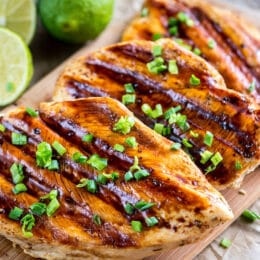 grilled chicken breasts with coconut and lime marinade on a wooden cutting board with fresh limes in the background
