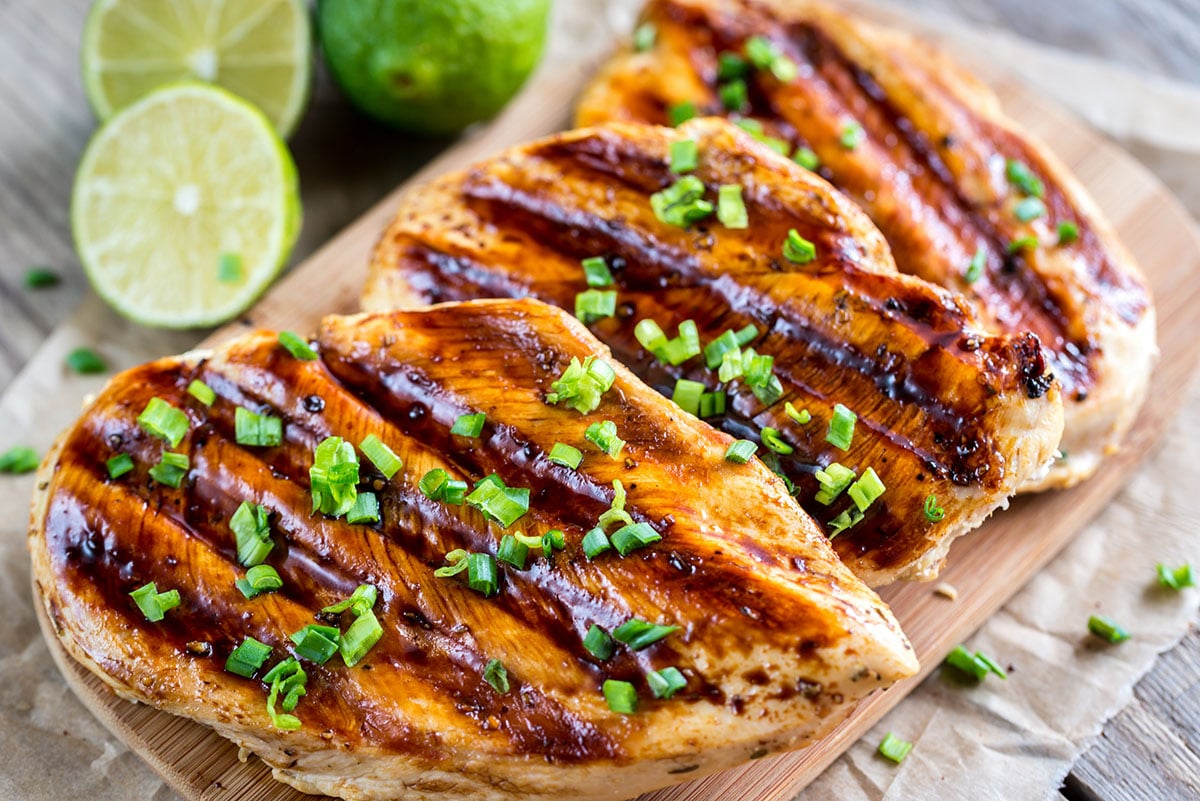 grilled chicken breast with a coconut-lime marinade on a wooden cutting board with fresh limes in the background