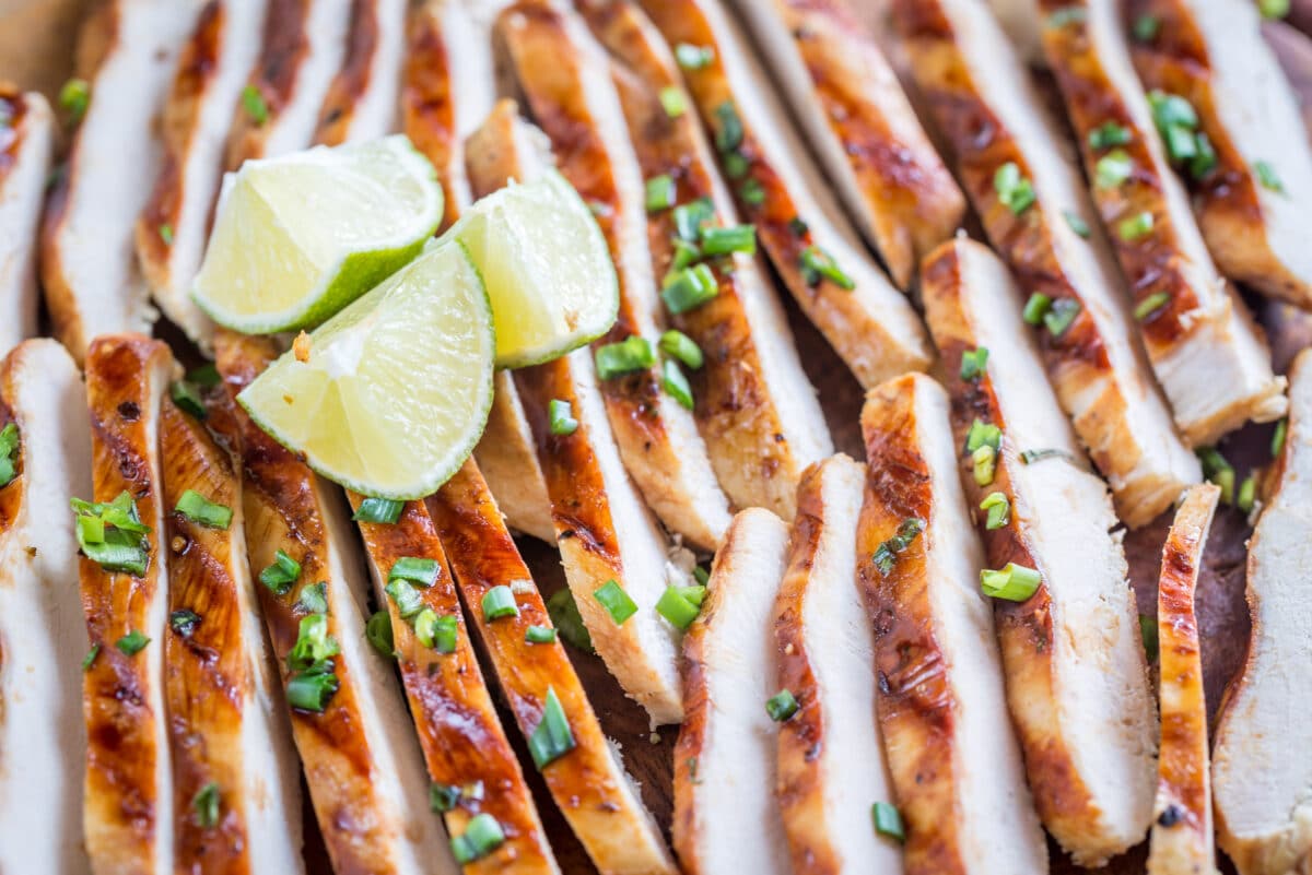 slices of grilled chicken breast with a coconut lime marinade on a wooden cutting board with fresh limes on top