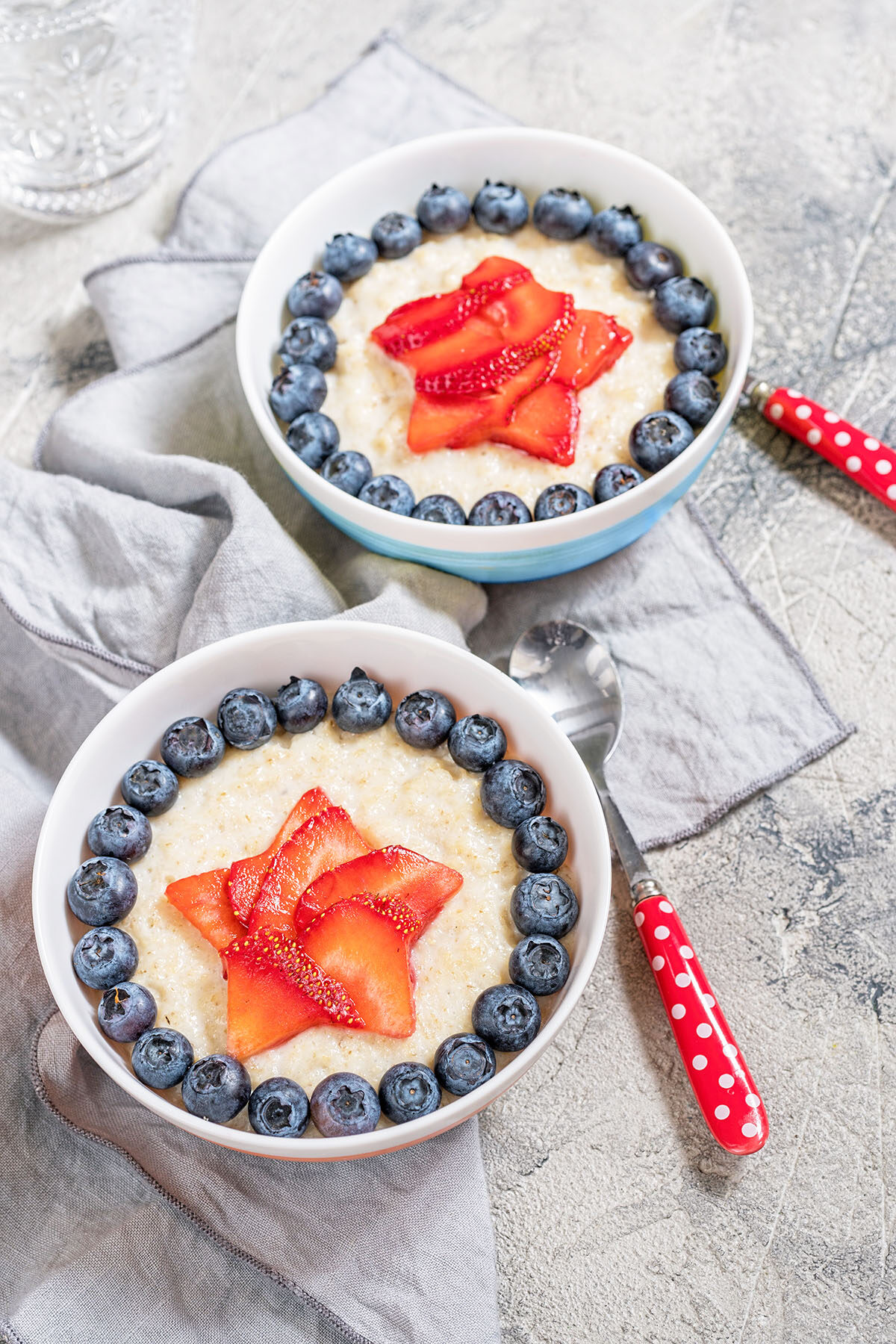 cream of wheat in bowls with strawberries and blueberries in a patriotic star pattern with red polka dot spoons and paper cutout stars in the background