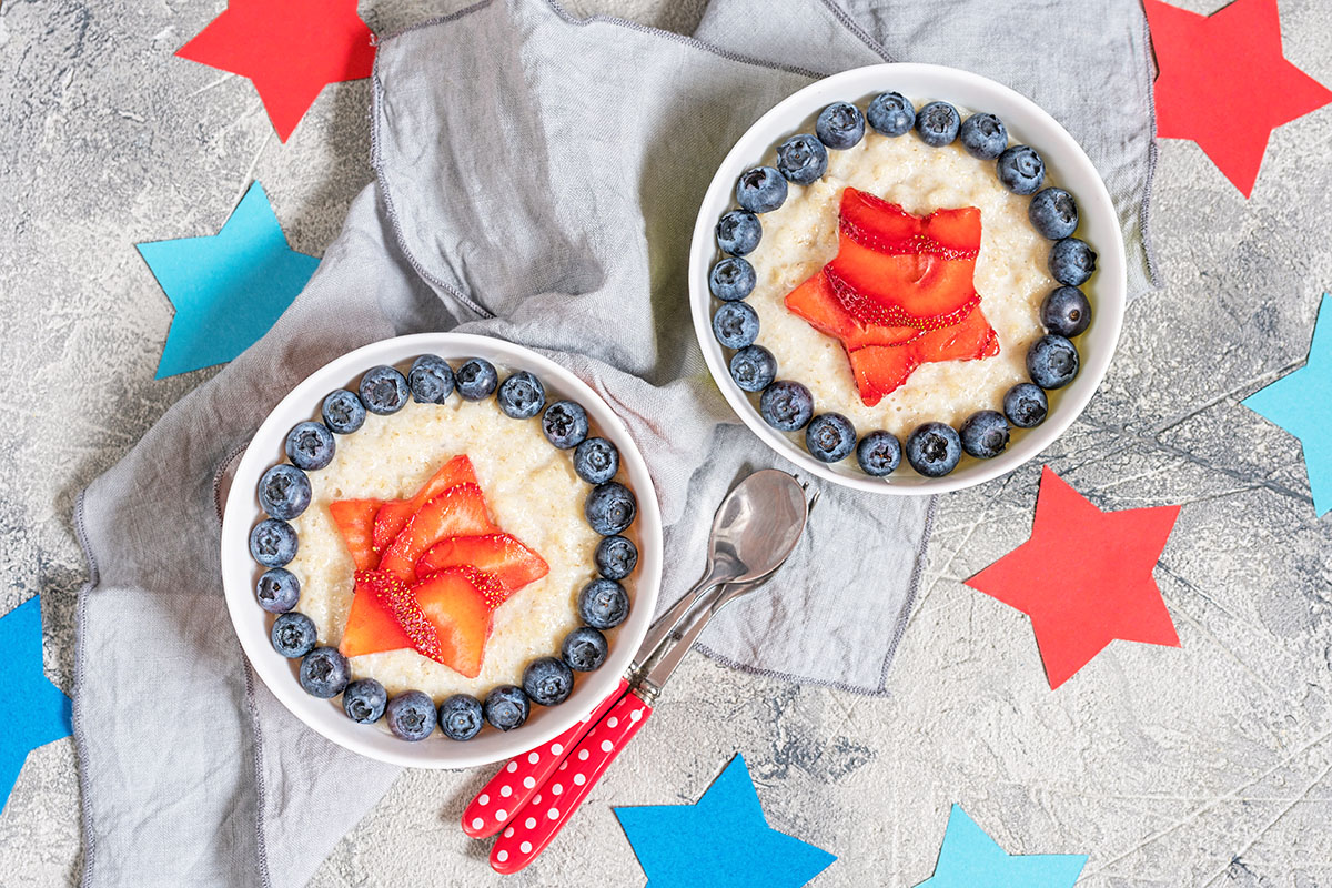 cream of wheat in bowls with strawberries and blueberries in a patriotic star pattern with red polka dot spoons and paper cutout stars in the background