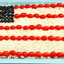layered bean dip that looks like an American flag with tomatoes, mozzarella cheese and olives