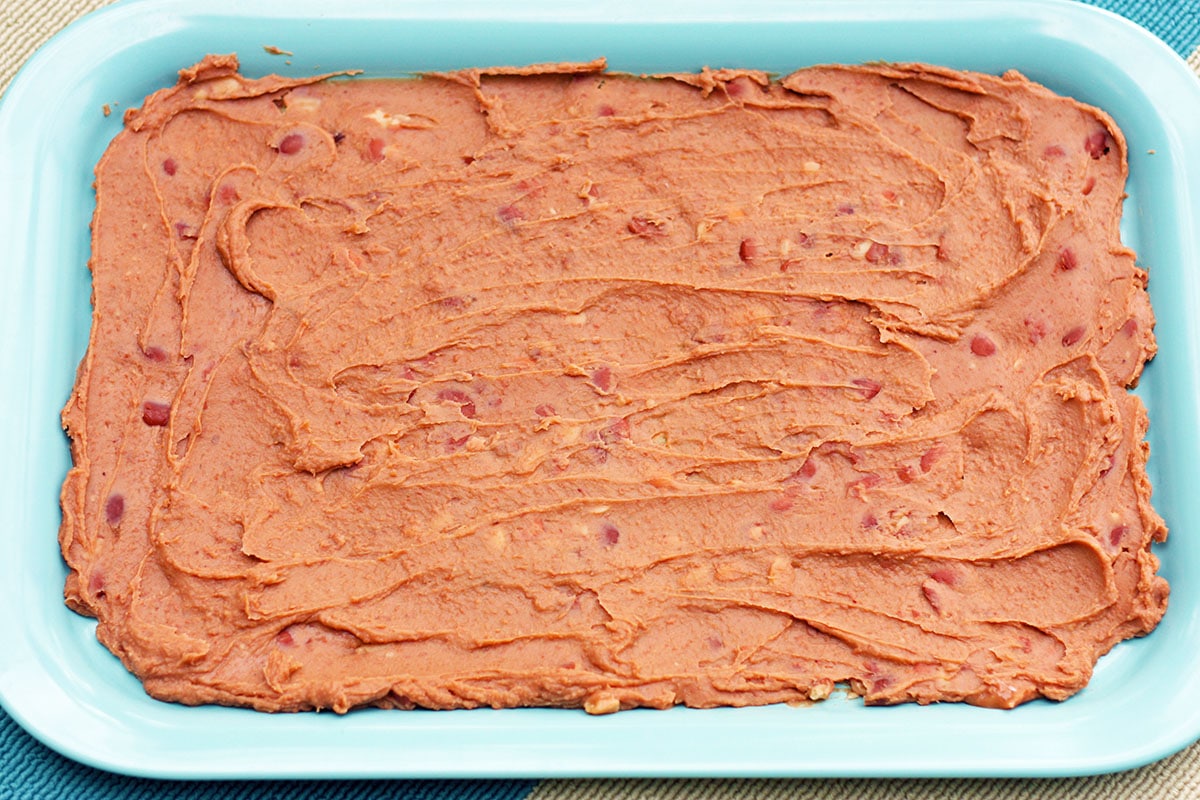 refried beans on a blue tray as the first layer of layered bean dip