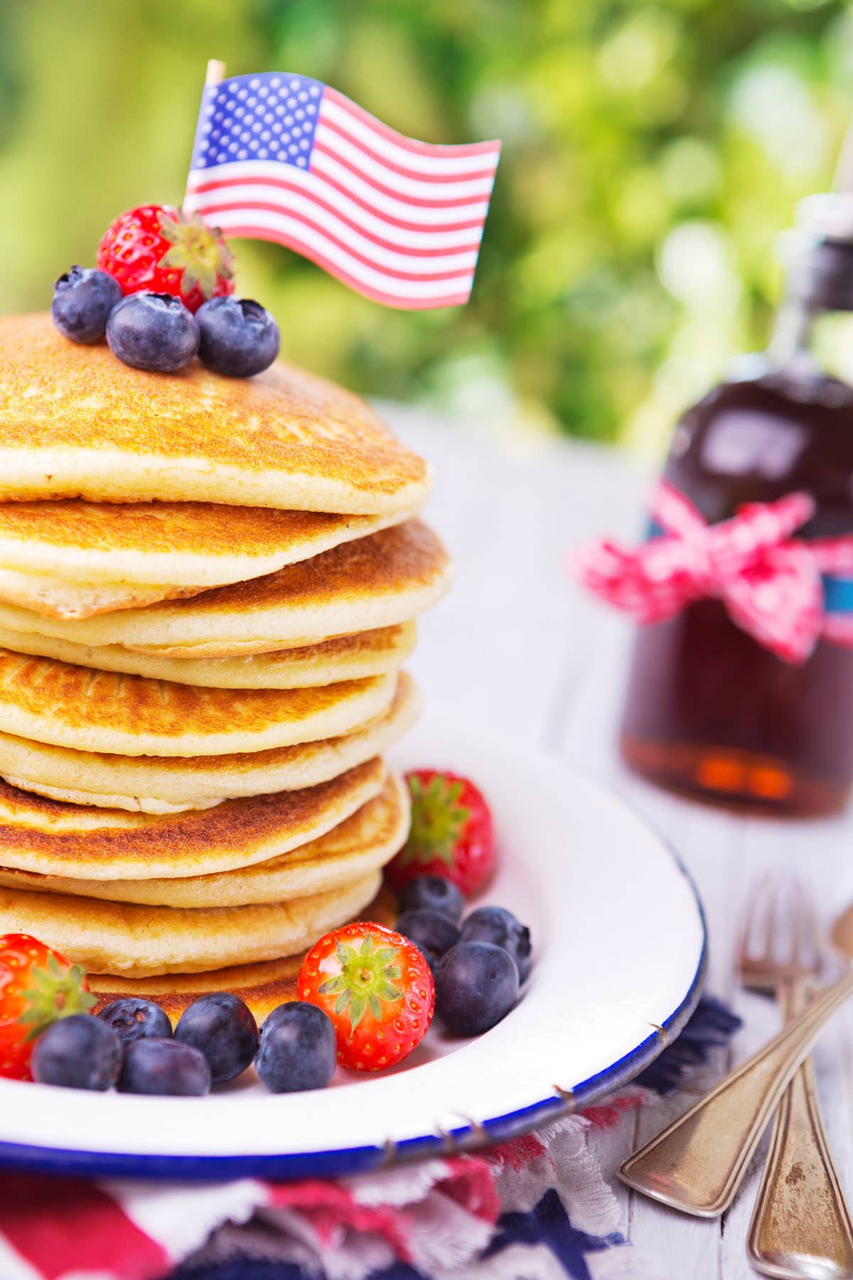 A stack of homemade whole grain pancakes with fresh berries, butter and syrup and an american flag on top