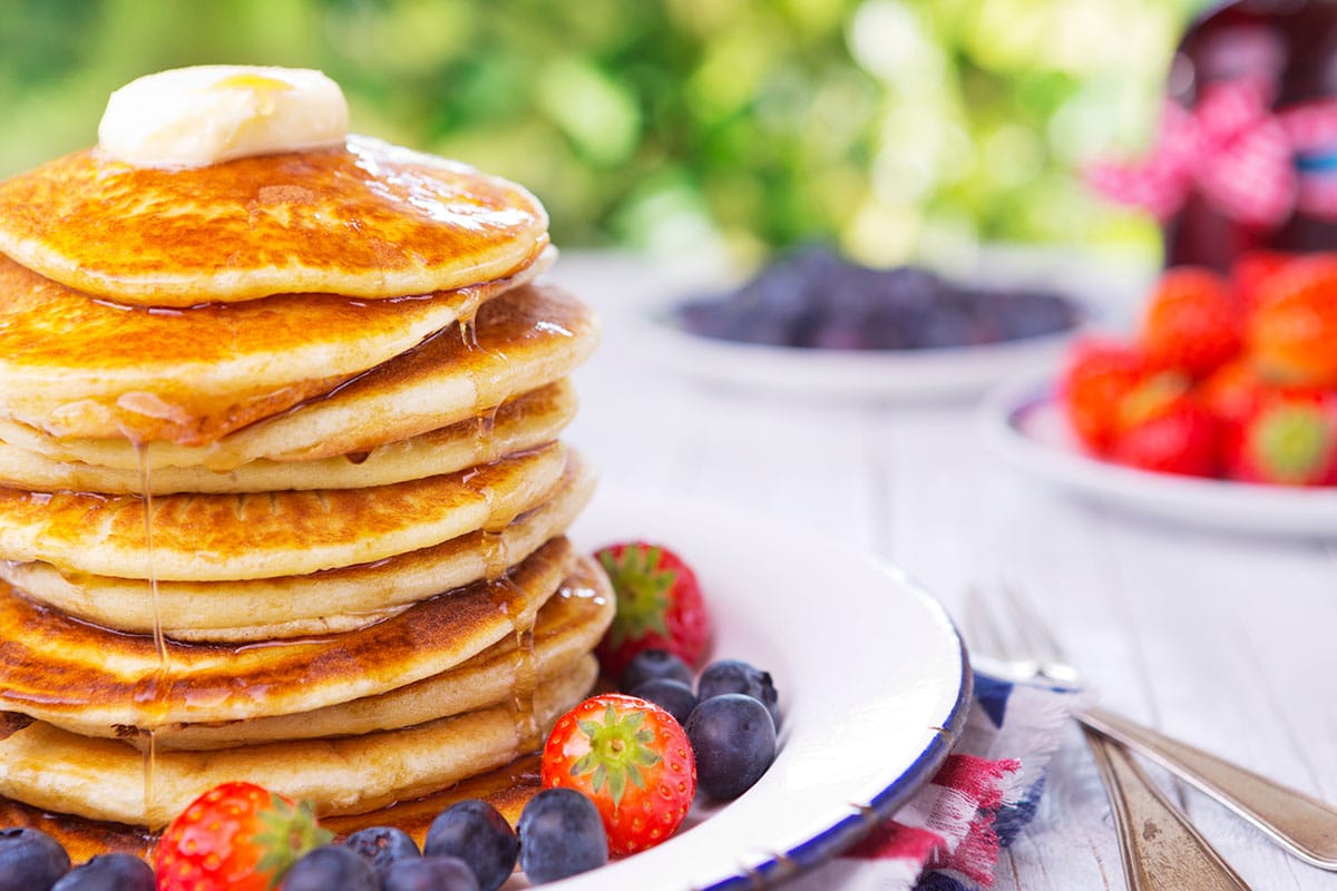 A stack of homemade whole grain pancakes with fresh berries, butter and syrup and an american flag on top