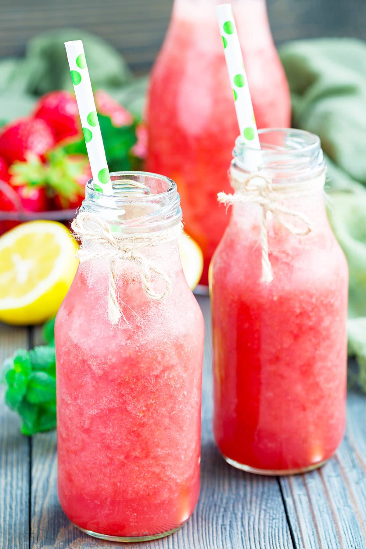 Homemade fresh strawberry lemonade with fresh strawberries, lemon, ice and mint in glass bottle, vertical