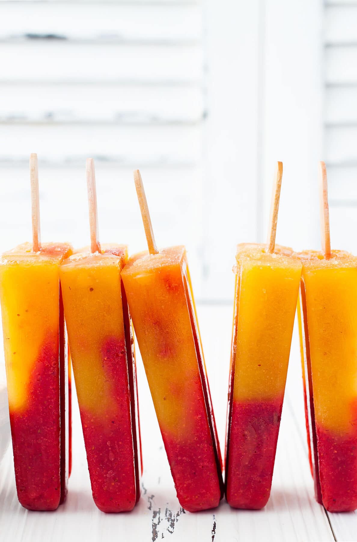strawberry mango popsicles standing on a white plate