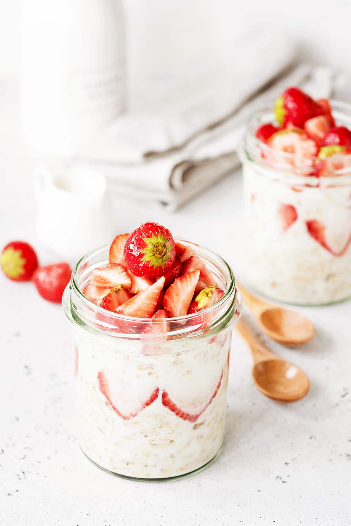 healthy strawberry overnight oats in a glass jar with wooden spoons and another glass jar in the background