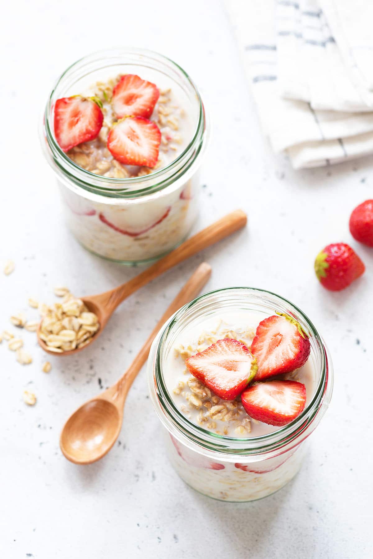 overnight oats with strawberries in mason jars overhead view with two wooden spoons with oats on them