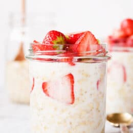 Overnight oats with strawberries in a glass jar with a golden spoon and another mason jar in the background