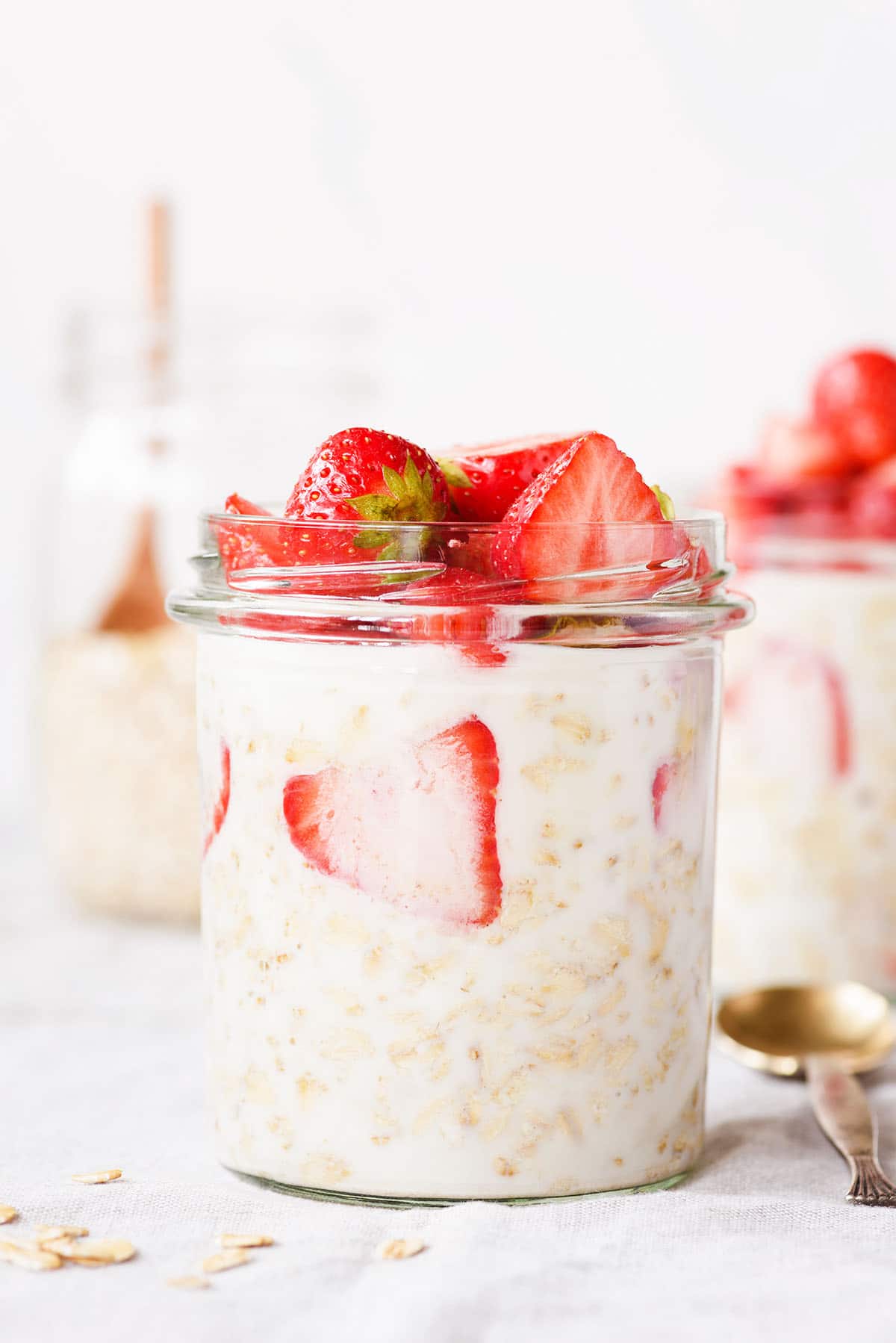 overnight oats in a glass mason jar with strawberries and a gold spoon and more jars in the background