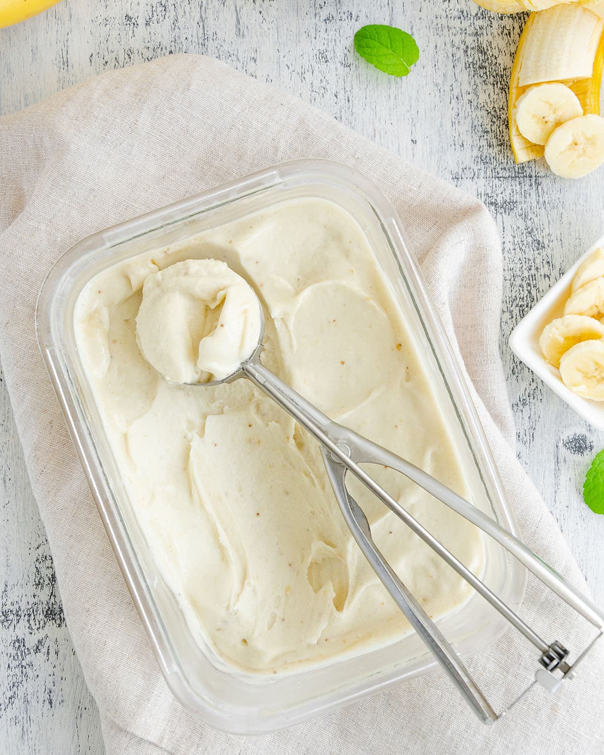 Homemade banana ice cream in a glass container with a spoon for ice cream on a wooden background. Healthy dessert.