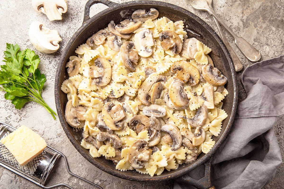 creamy mushroom pasta in a cast iron skillet with parmesan cheese, parsley and mushrooms in the background.