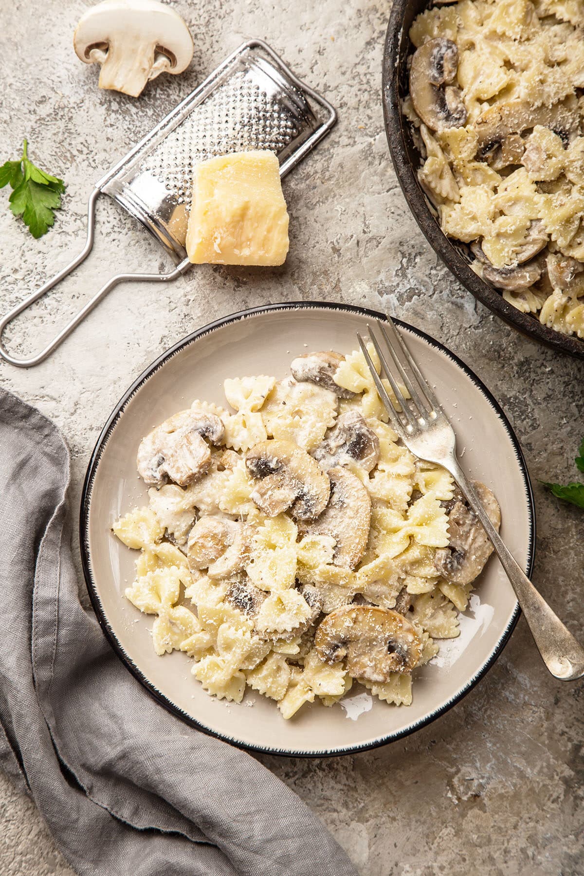 creamy mushroom pasta in a cast iron skillet with parmesan cheese, parsley and mushrooms in the background.  Plate of mushroom pasta with a fork on the plate. 