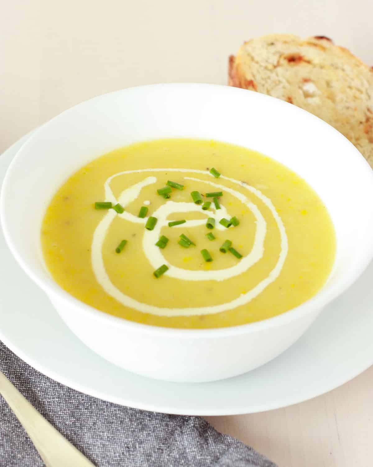 creamy yellow squash soup with a metal spoon and sourdough bread on the sides, green chives on top as a garnish