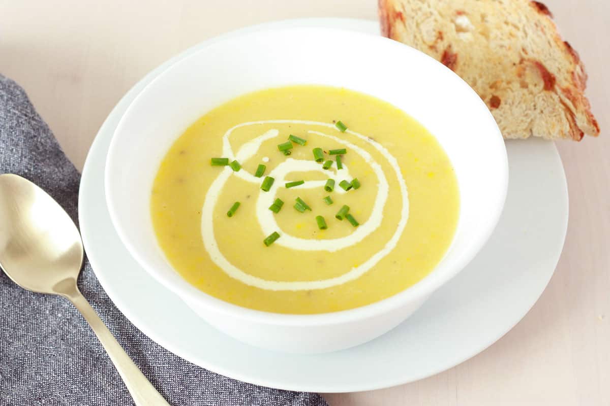 creamy yellow squash soup with a metal spoon and sourdough bread on the sides, green chives on top as a garnish