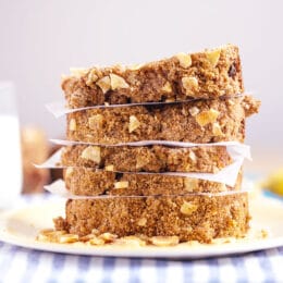 healthy banana bread with streusel topping stacked in slices on a yellow plate with a glass of milk and bananas in the background