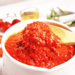 thick tomato pasta sauce in a white pot with a wooden spoon lifting the sauce out of the pot.