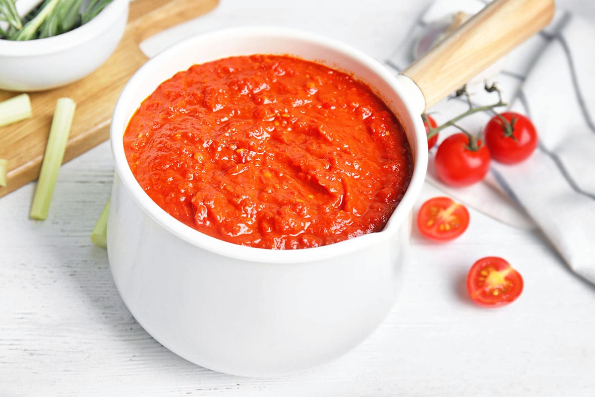 marinara pasta sauce in a white pot with tomatoes and herbs in the background