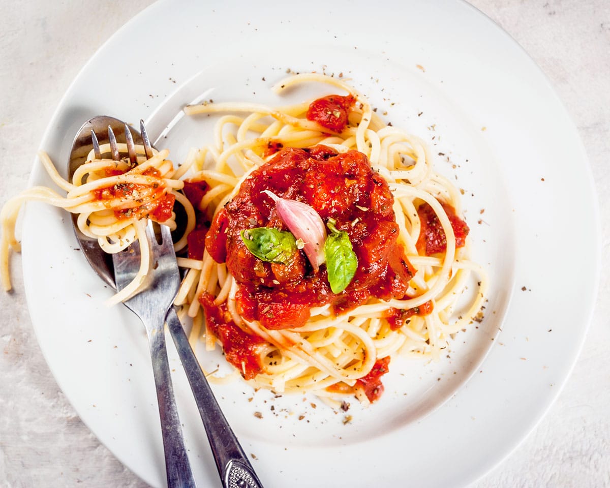 A serving of spaghetti pasta with tomato pasta sauce and basil on a white concrete table.