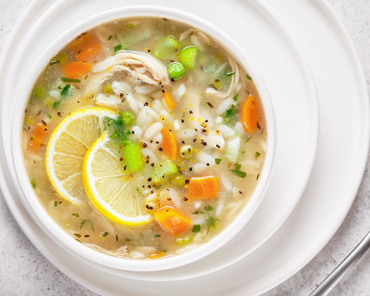 bowl of lemon chicken orzo soup with carrots, celery, peas and chicken with lemon slices and fresh parsley