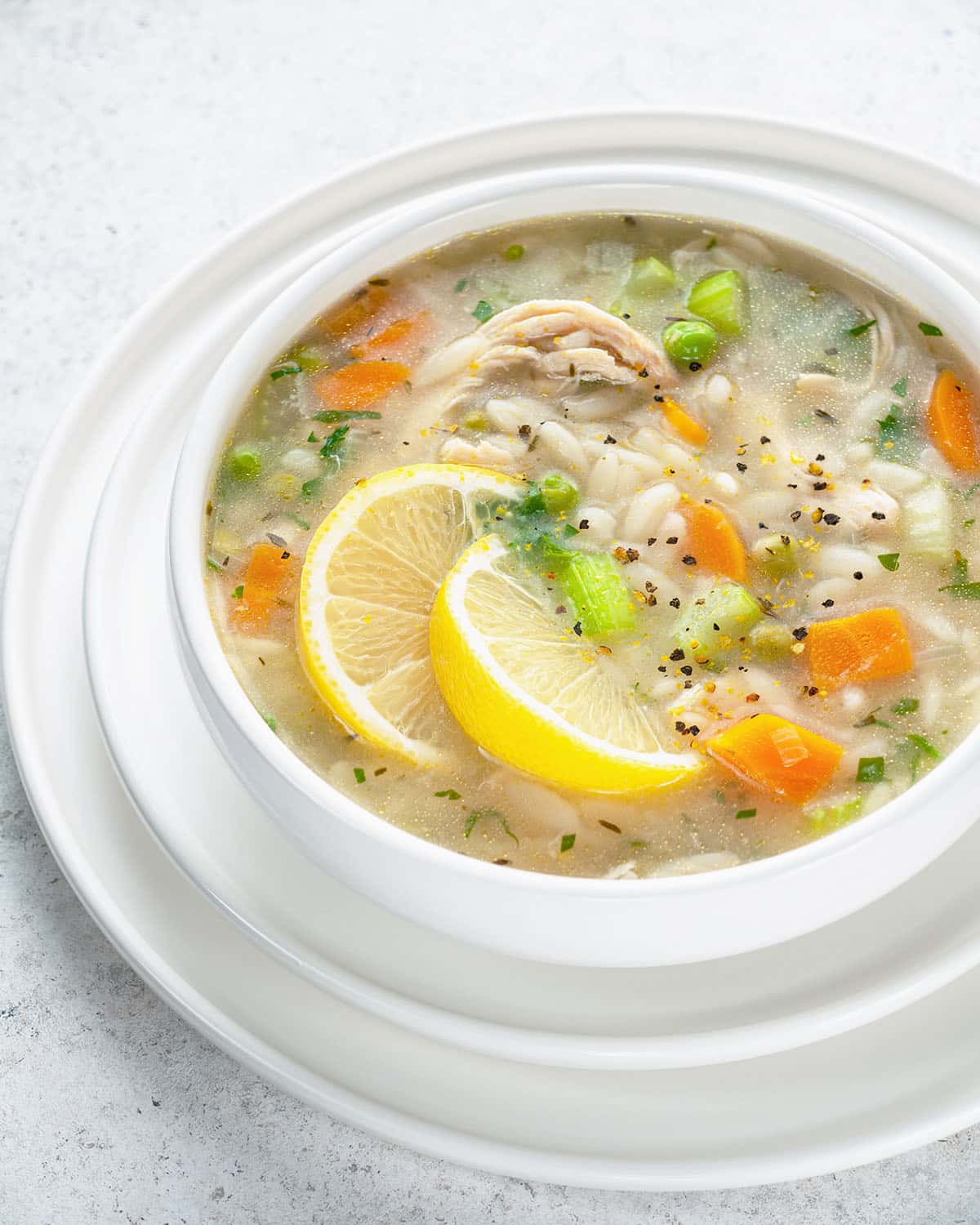 lemon chicken orzo soup in a white bowl with carrots, chicken, celery and lemon slices