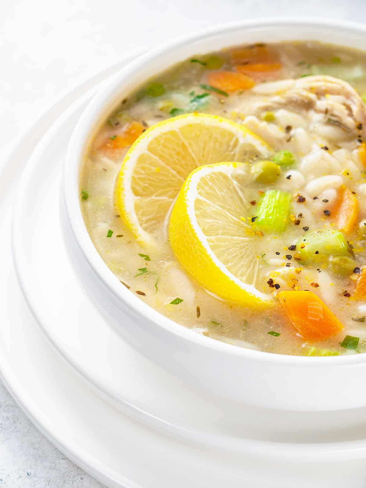 bowl of lemon chicken orzo soup with carrots, celery, peas and chicken with lemon slices and fresh parsley