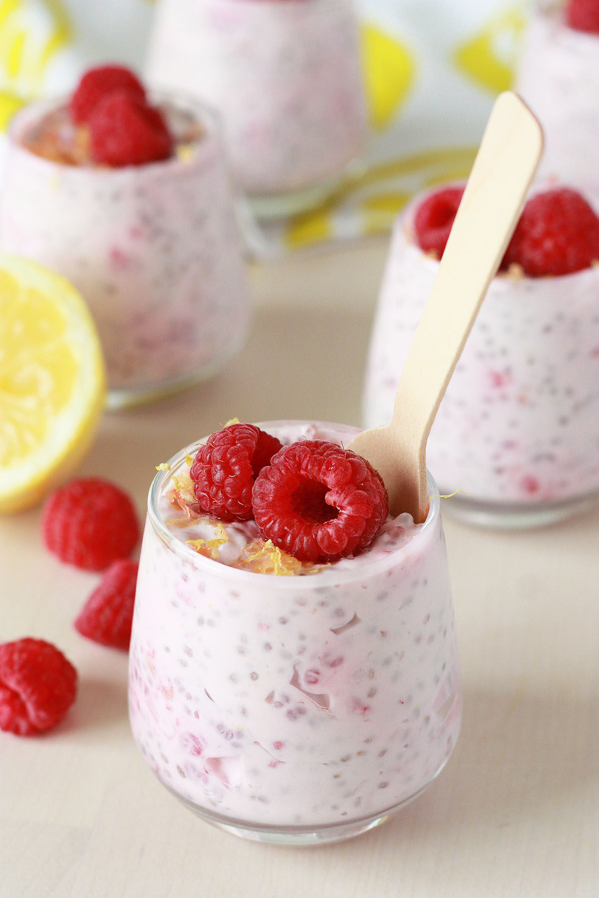 closeup view of chia seed pudding with lemon and raspberries in a small glass jar on a wood table