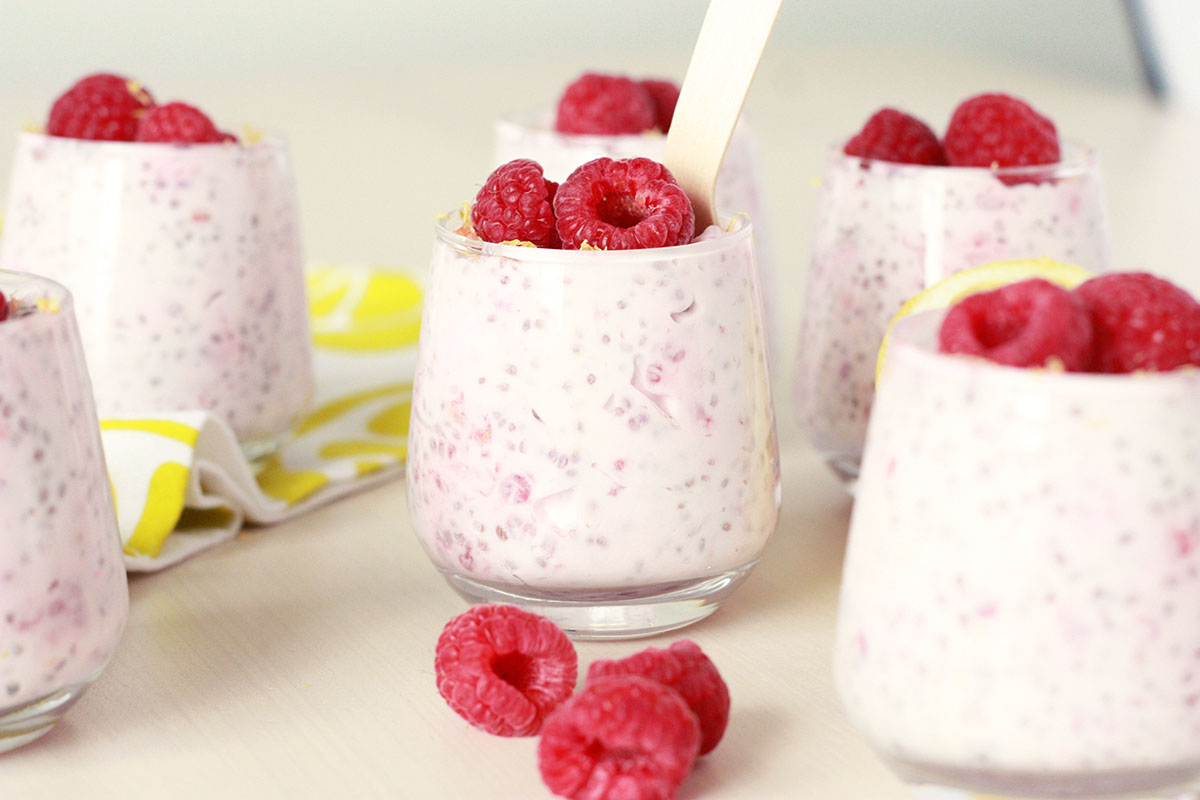 lemon raspberry chia seed pudding in small glass jars with fresh raspberries and lemon zest on top with a small silver spoon in the jar and a fresh lemon in the background