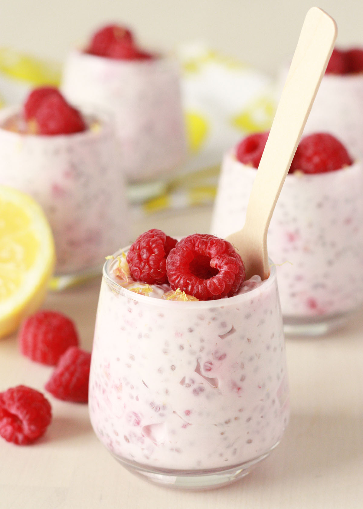 lemon raspberry chia seed pudding in small glass jars with fresh raspberries and lemon zest on top with a wooden spoon in the jar