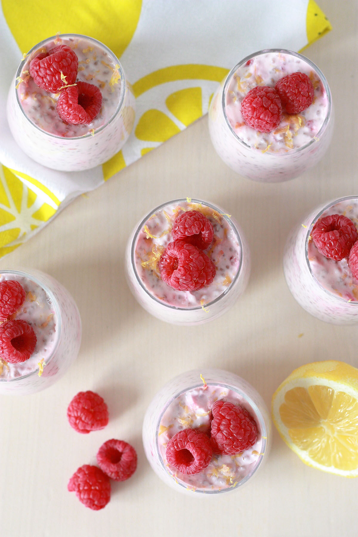 overhead view of lemon raspberry chia seed pudding in small glass jars with fresh raspberries and lemon zest on top