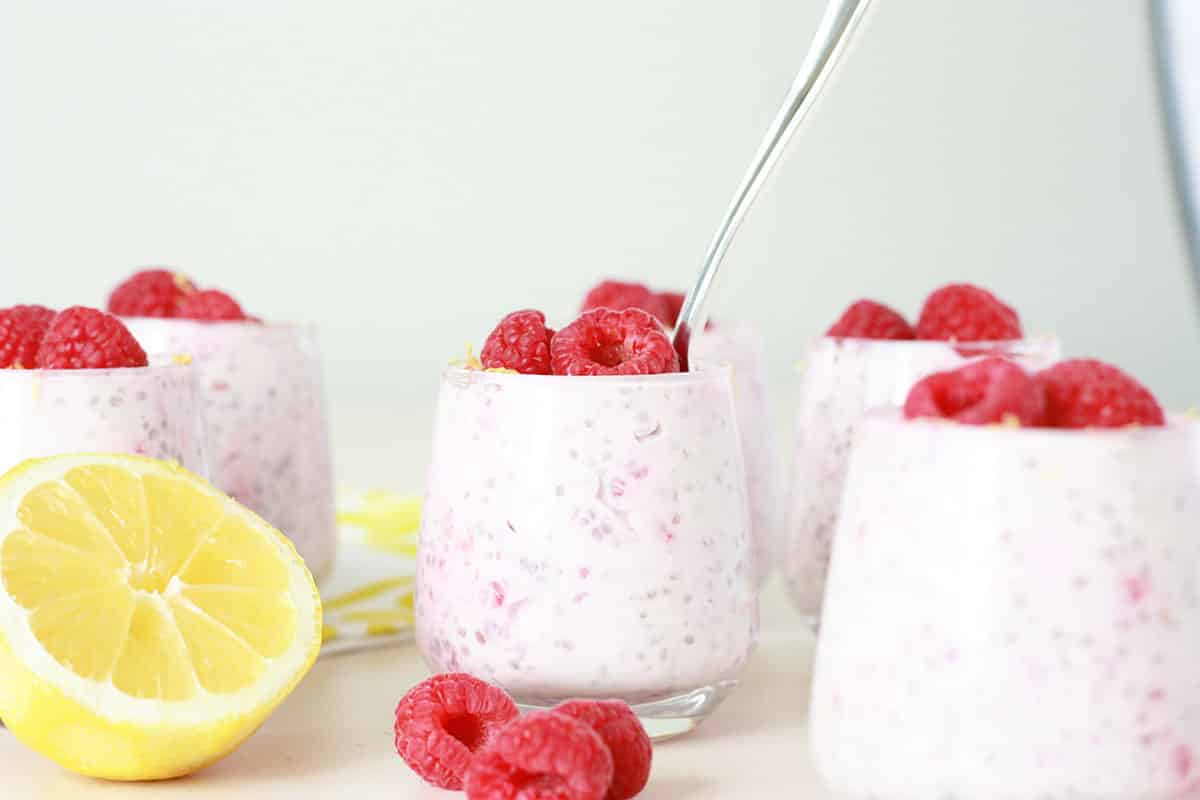 lemon raspberry chia seed pudding in small glass jars with fresh raspberries and lemon zest on top with a small silver spoon in the jar and a fresh lemon in the background