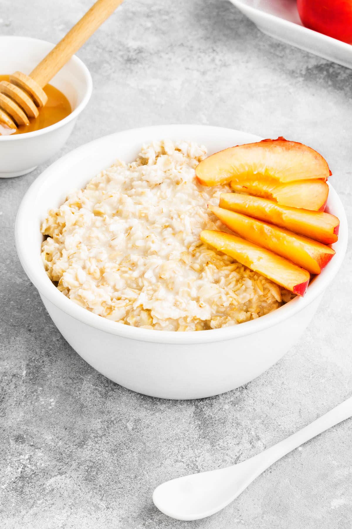 peaches and cream oatmeal with fresh sliced peaches in a white bowl and honey in the background